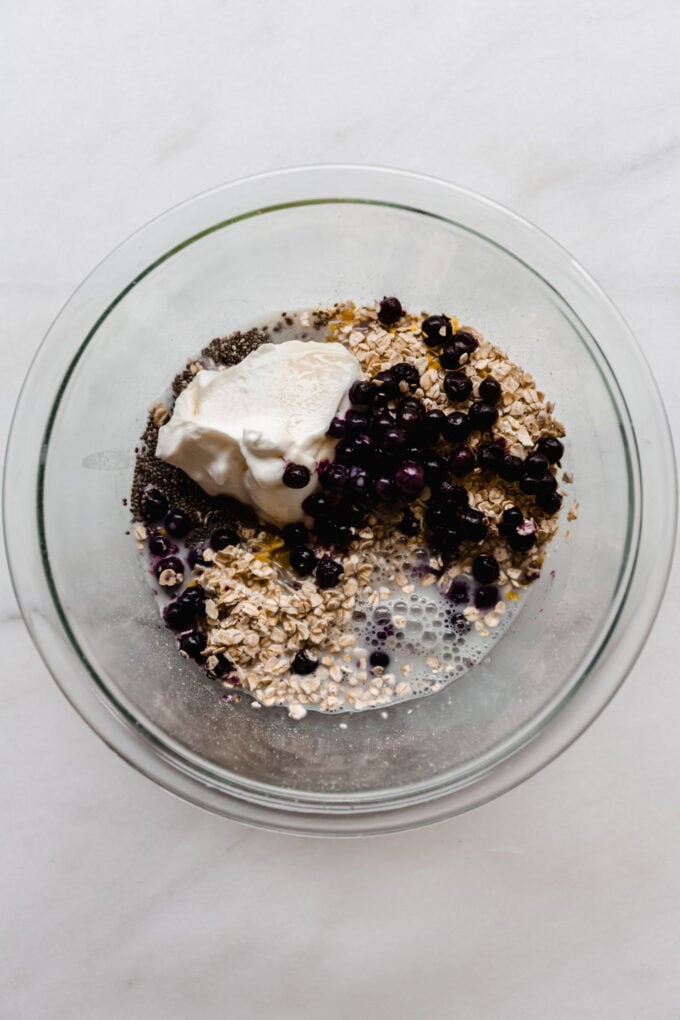 oats, chia seeds, yogurt, blueberries and almond milk in a clear mixing bowl.