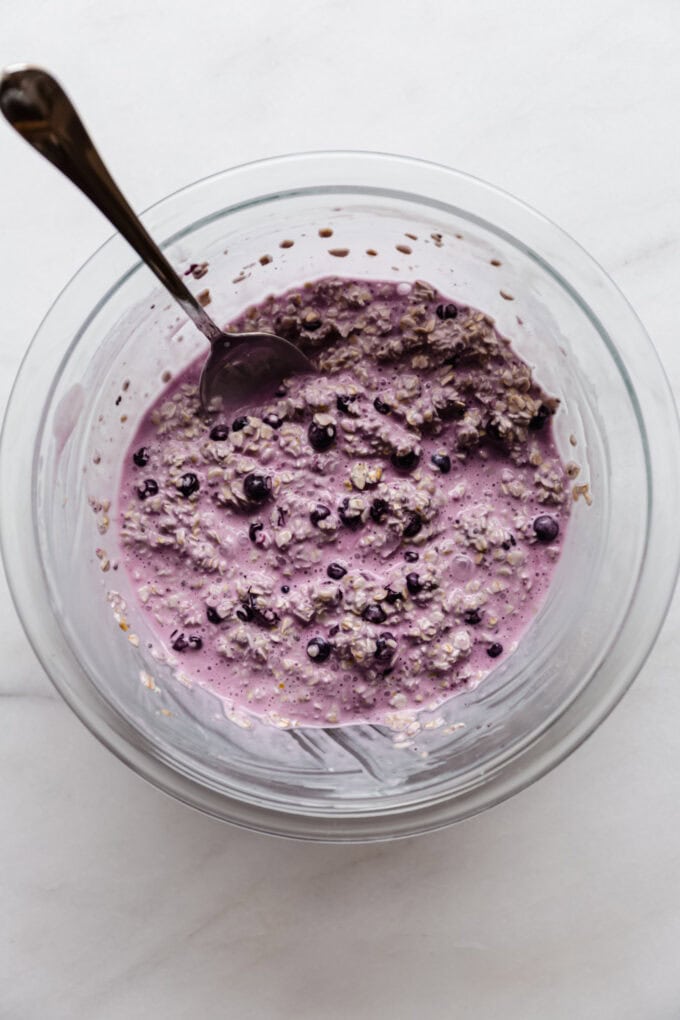 blueberry overnight oats before setting in the fridge in a clear mixing bowl with a spoon in it.