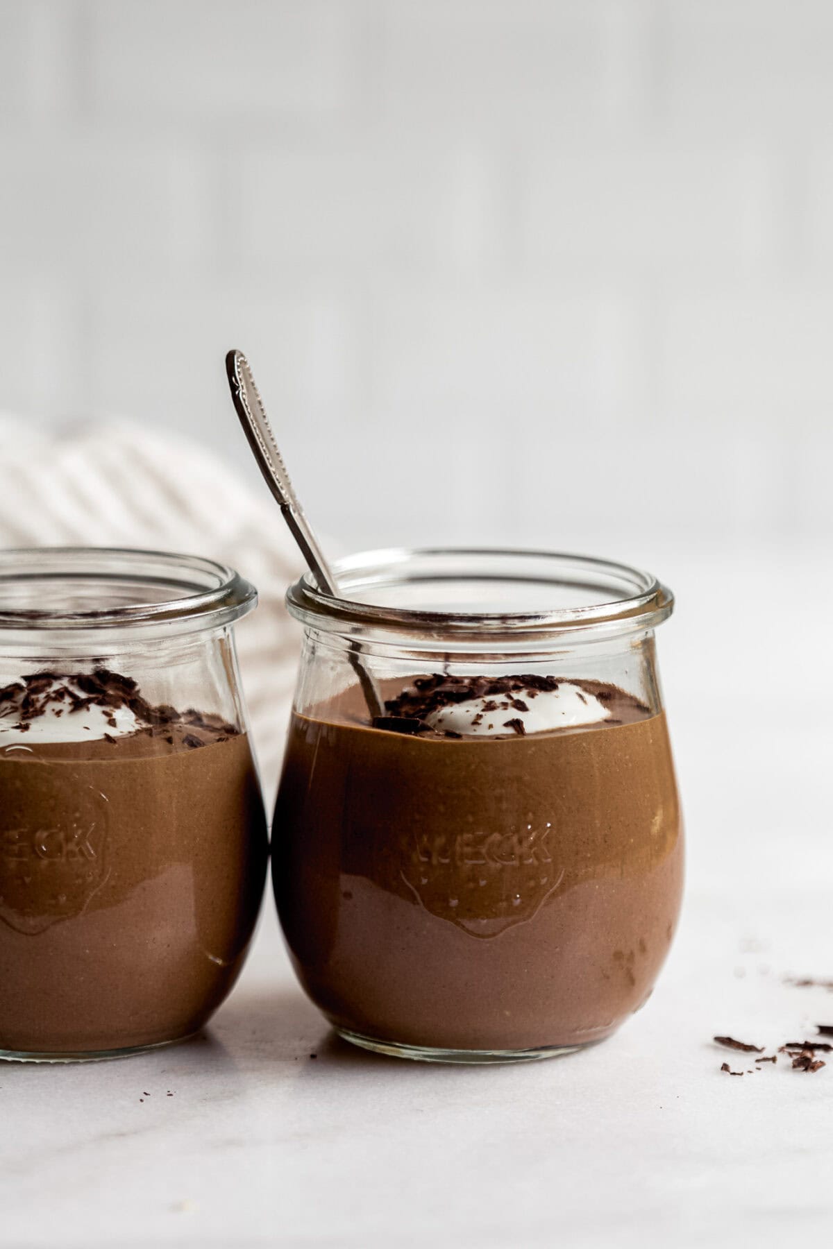 two cups of cottage cheese chocolate mousse in small jars on a marble countertop.