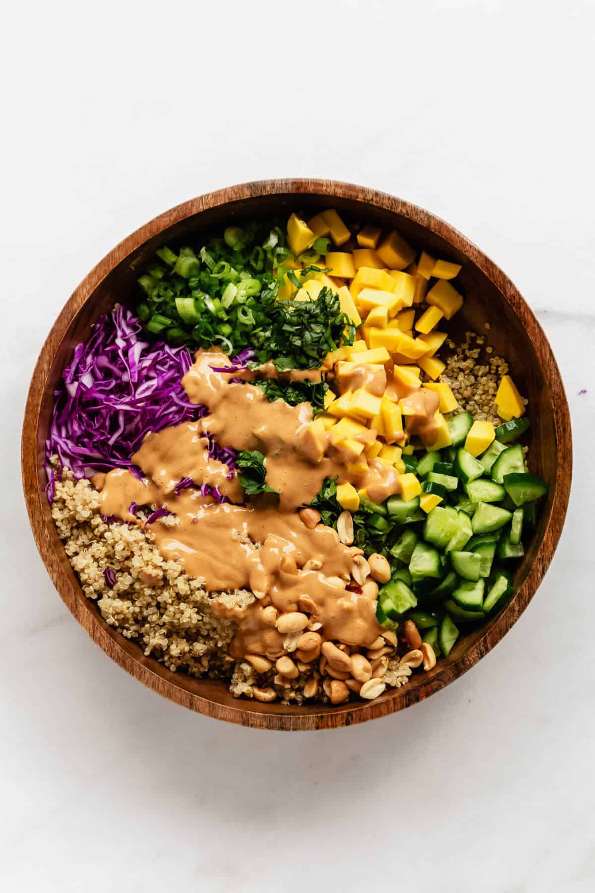 Thai quinoa salad in a wood salad bowl with peanut dressing poured over it.
