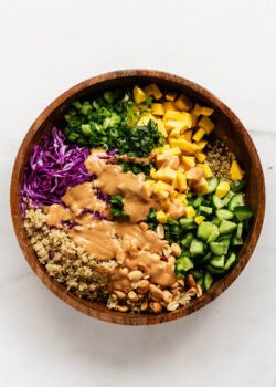 Thai quinoa salad in a wood salad bowl with peanut dressing poured over it.