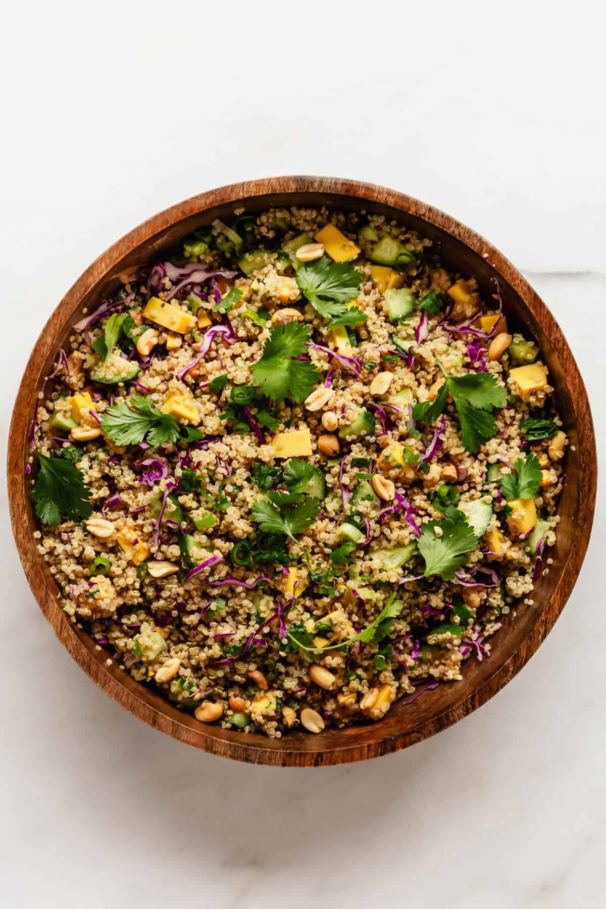 Thai quinoa salad in a wood mixing bowl topped with cilantro leaves.