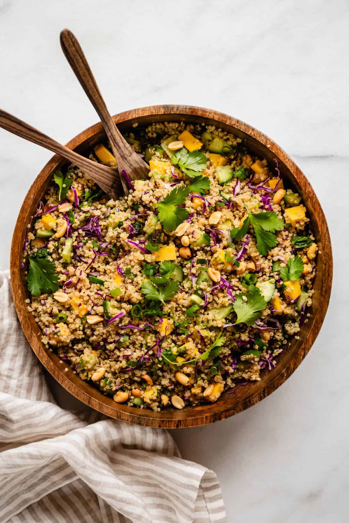 Thai quinoa salad in a wood salad bowl with wooden serving spoons.