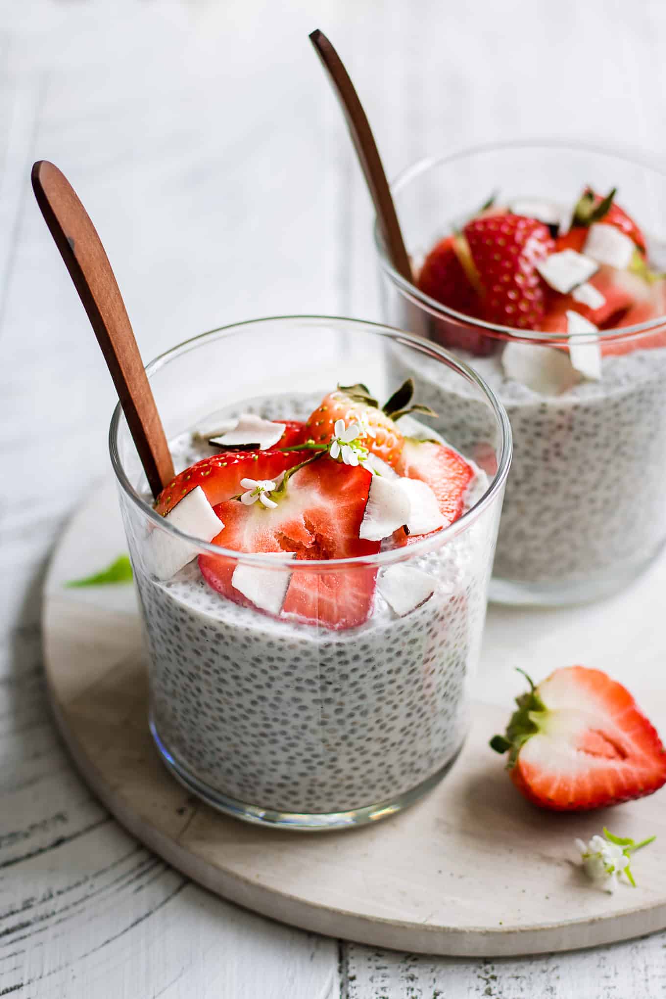 two cups of coconut chia pudding topped with strawberries on a marble board.