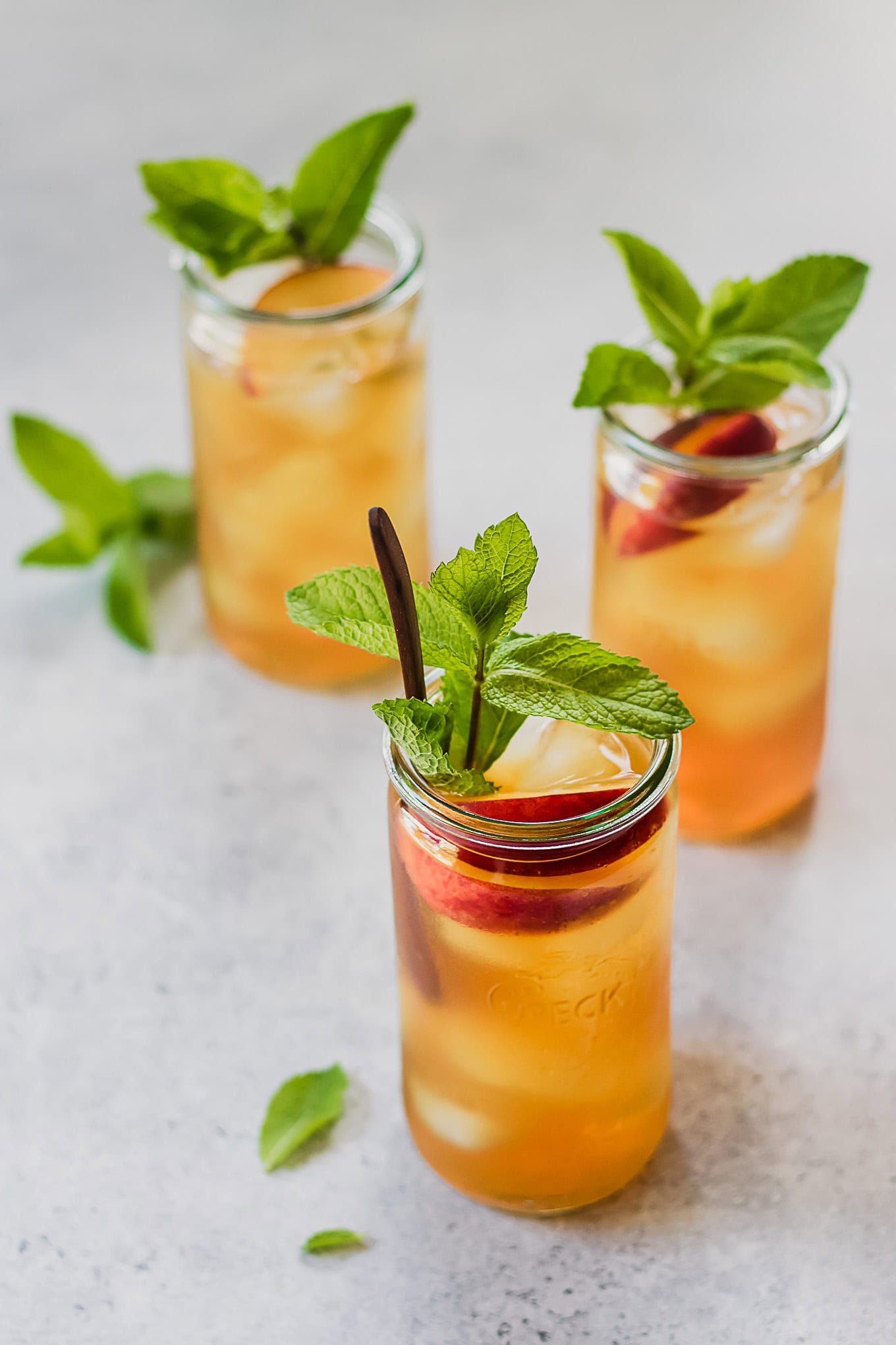 three jars of peach iced tea with mint sprigs.