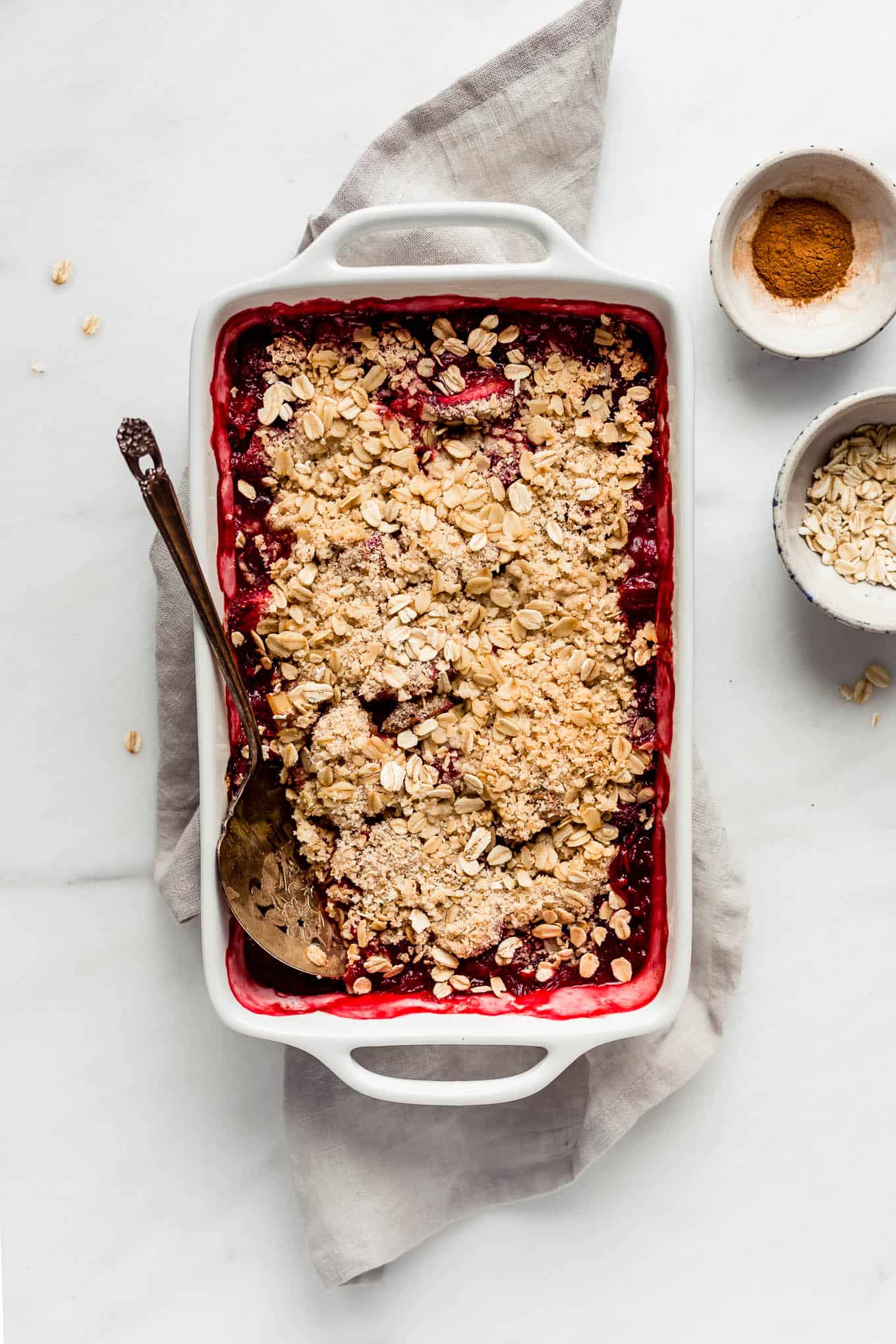 strawberry rhubarb crisp in a baking dish with a serving spoon.