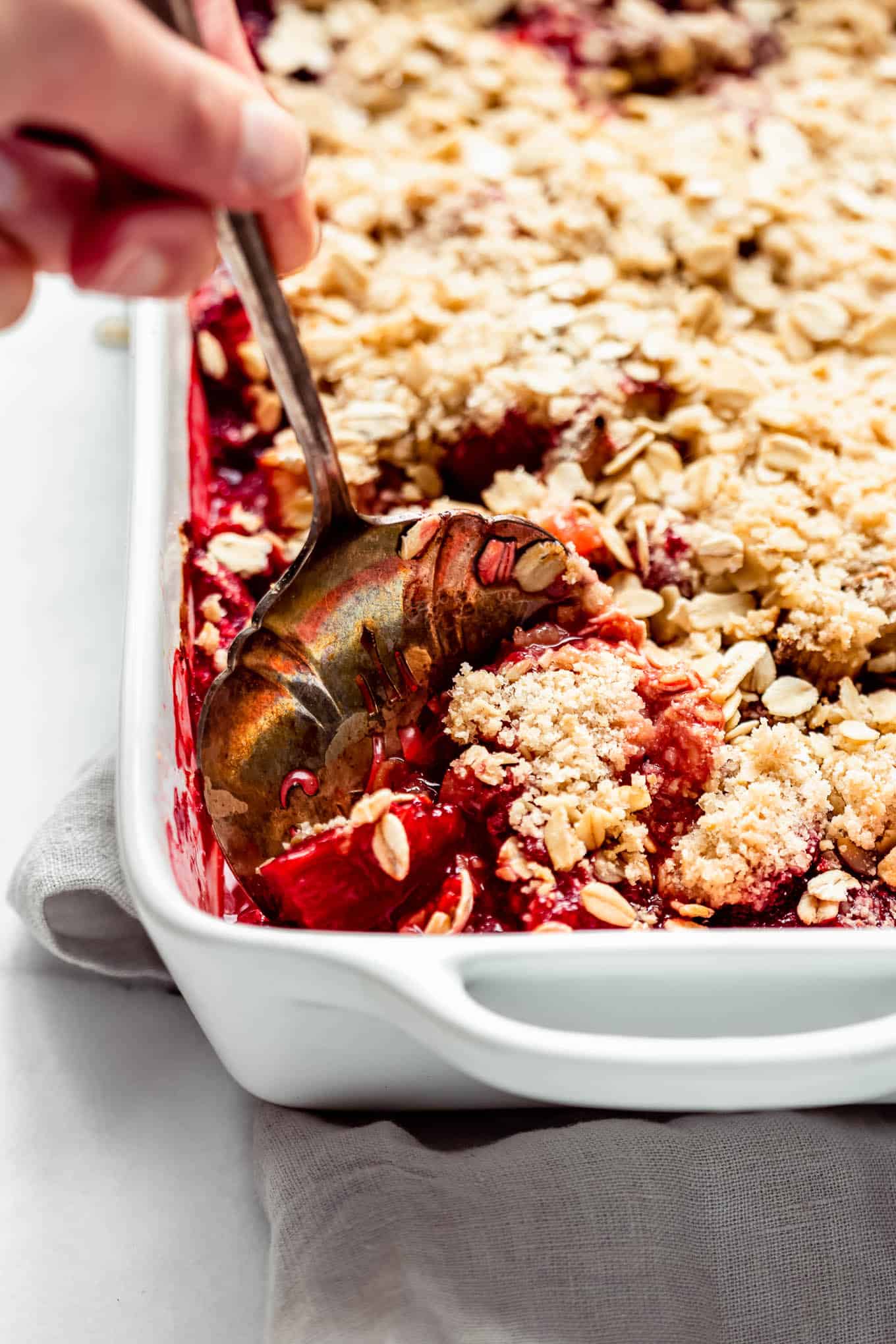 A hand scooping a piece of strawberry rhubarb crisp.