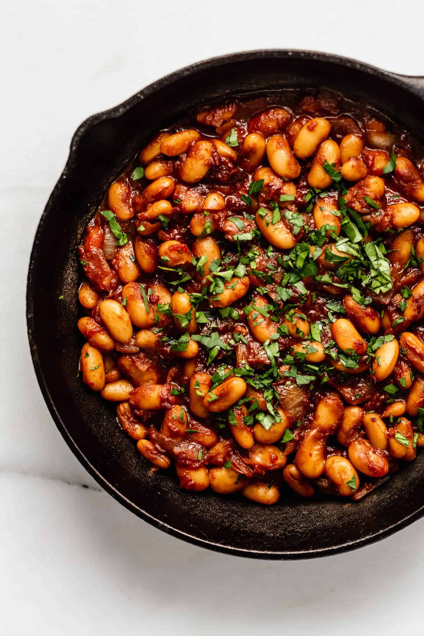 Maple baked beans in a cast iron skillet topped with herbs.