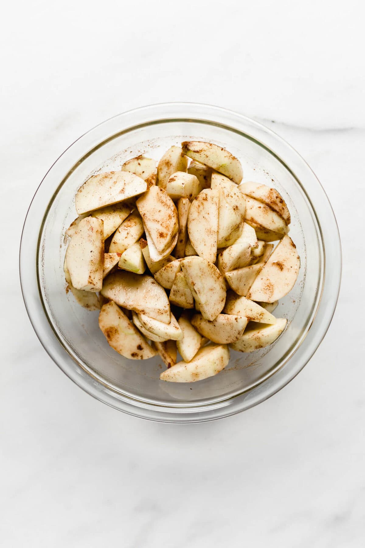 Sliced apples with cinnamon in a clear mixing bowl.