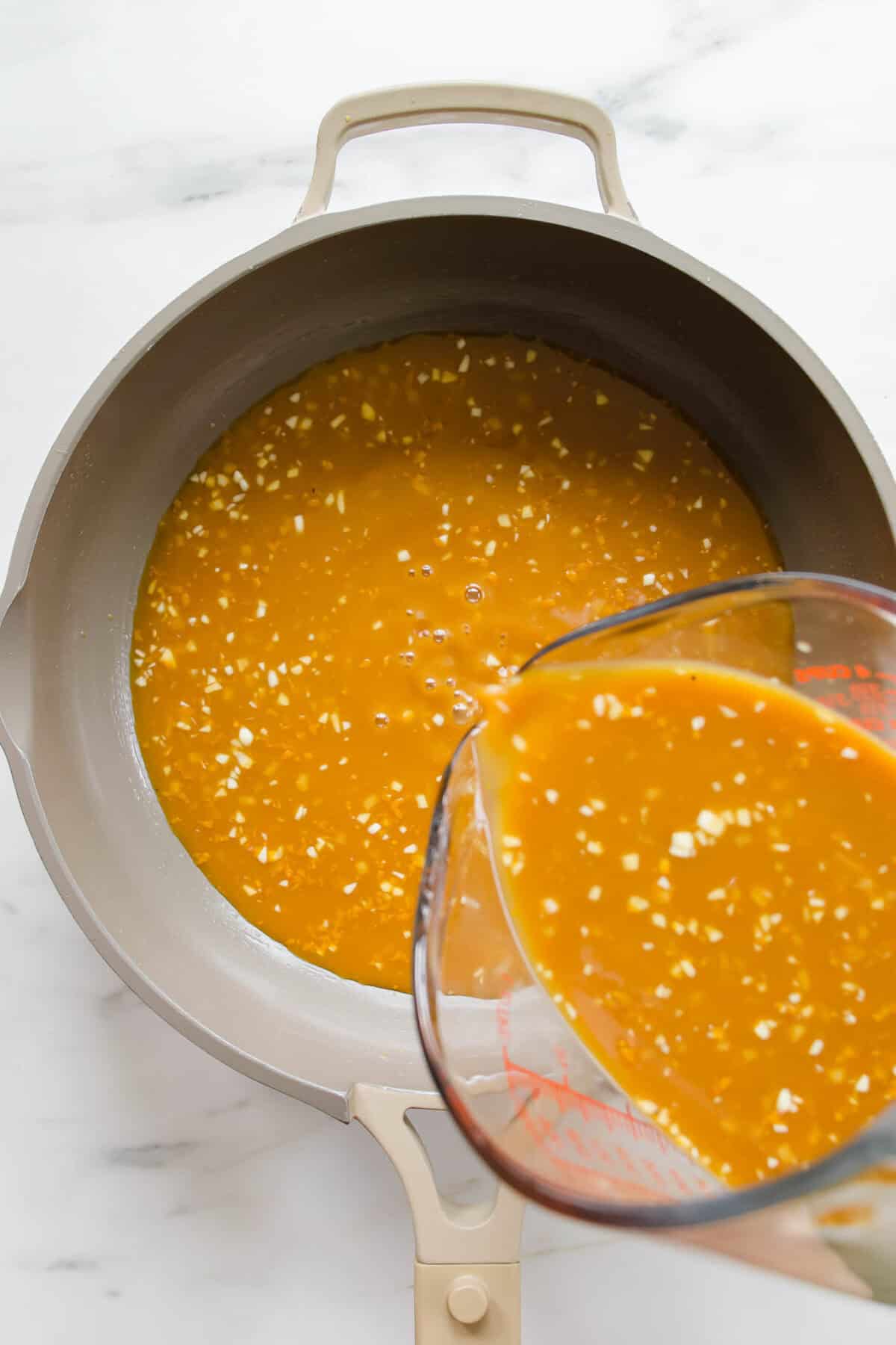 Orange sauce being poured into a pan.
