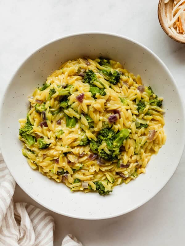 A bowl of broccoli cheddar orzo with a stripe napkin on the side.