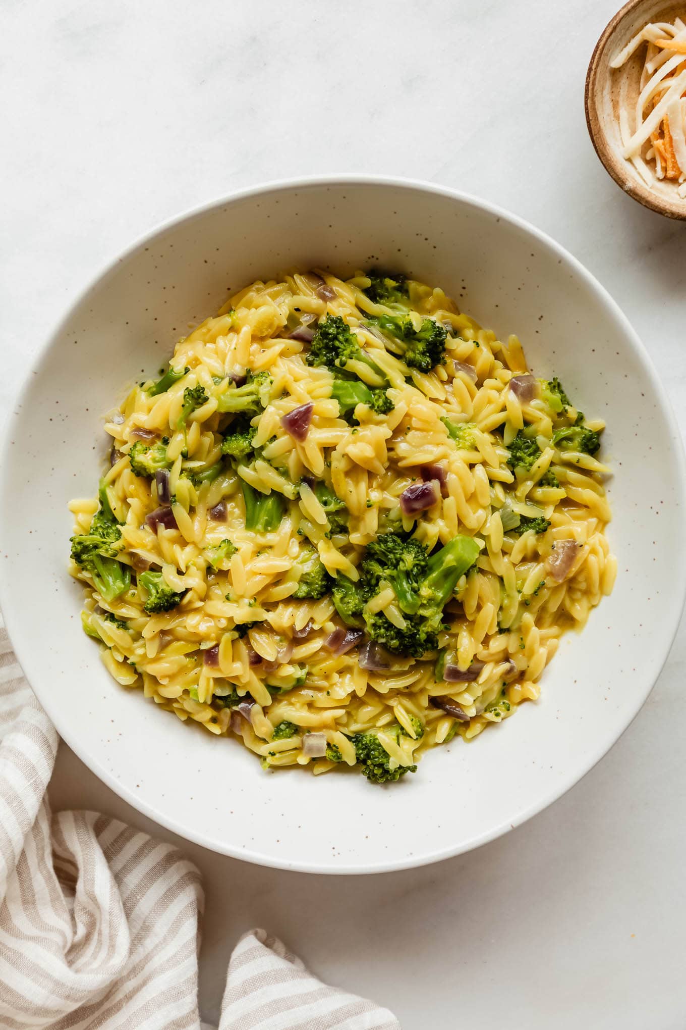 A bowl of broccoli cheddar orzo with a stripe napkin on the side.