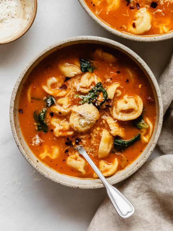 A bowl of tuscan tortellini soup with grated parmesan cheese on top.