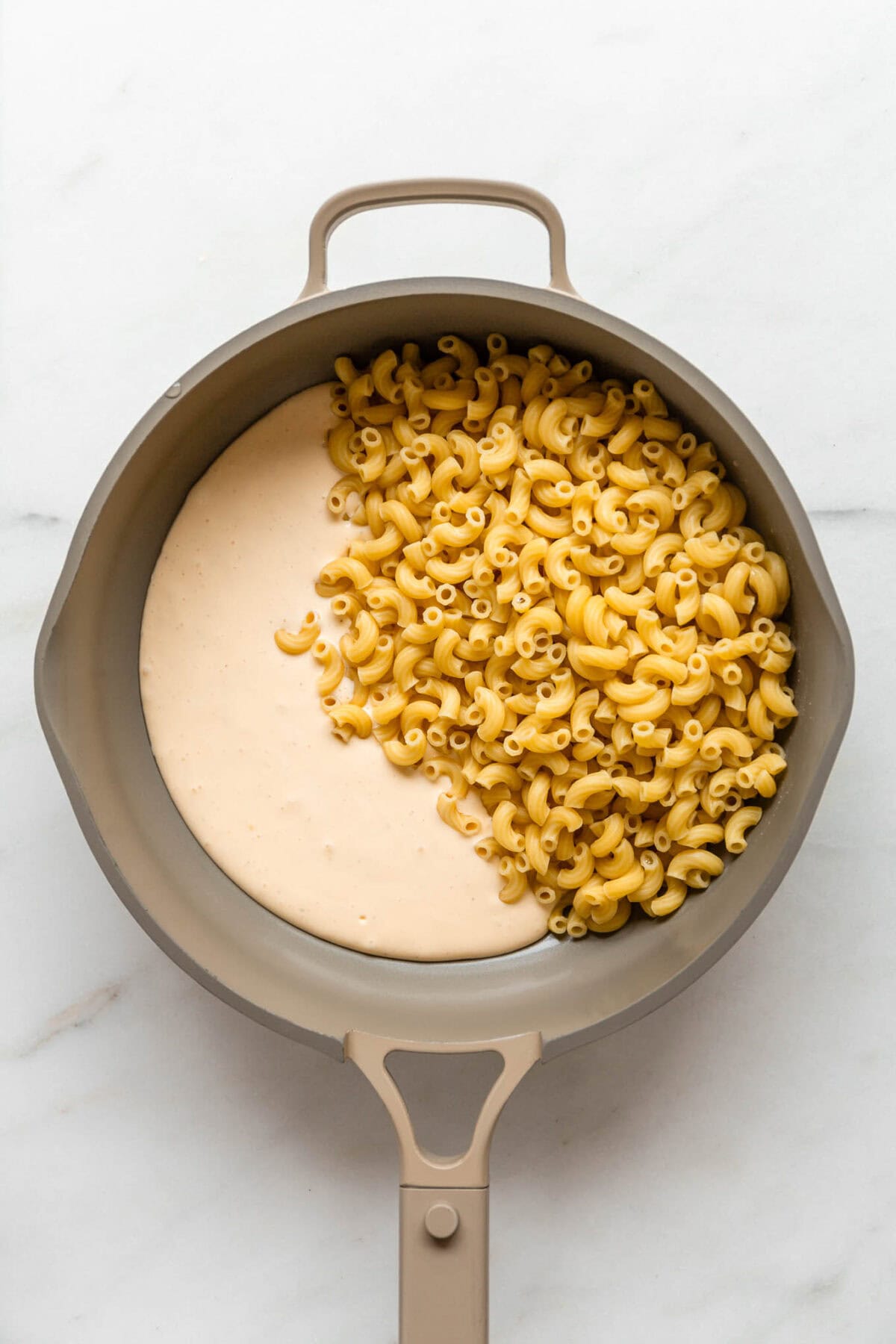 Macaroni noodles and cheese sauce in a taupe pan.