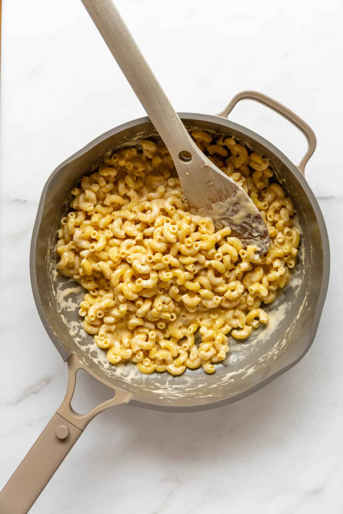 Cottage cheese mac and cheese in a beige pan with a wood spoon.