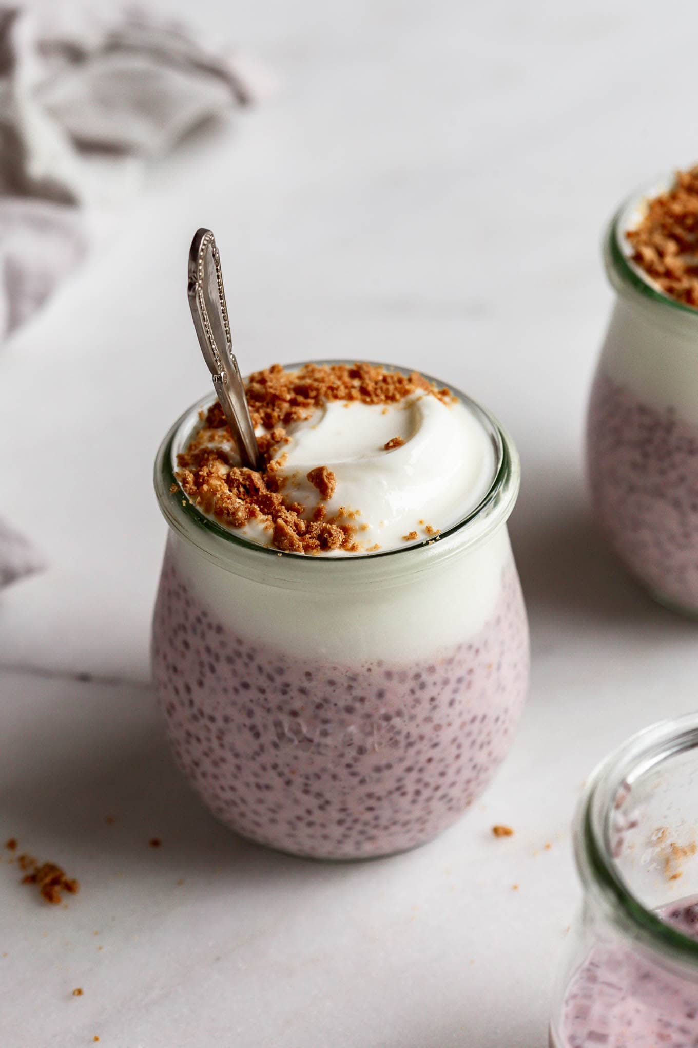 Protein chia pudding in a cup topped with graham cracker crumbs and a spoon in it.