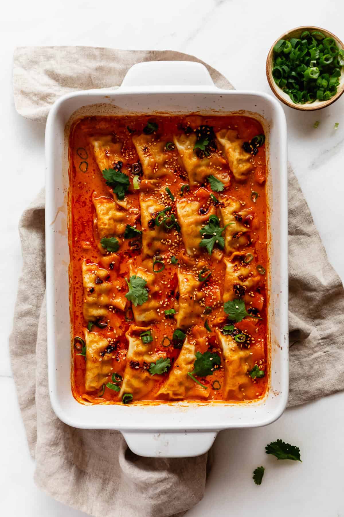 baked dumplings in bed curry sauce in a white baking dish on a beige napkin.