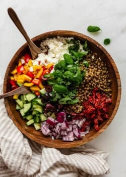 Mediterranean lentil salad in a wood bowl with wood spoons and a napkin on the side.