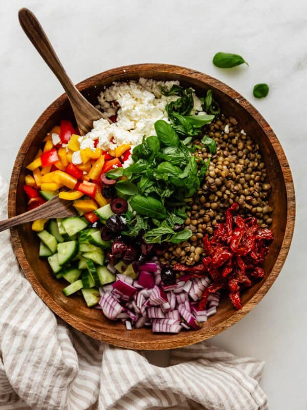 Mediterranean lentil salad in a wood bowl with wood spoons and a napkin on the side.