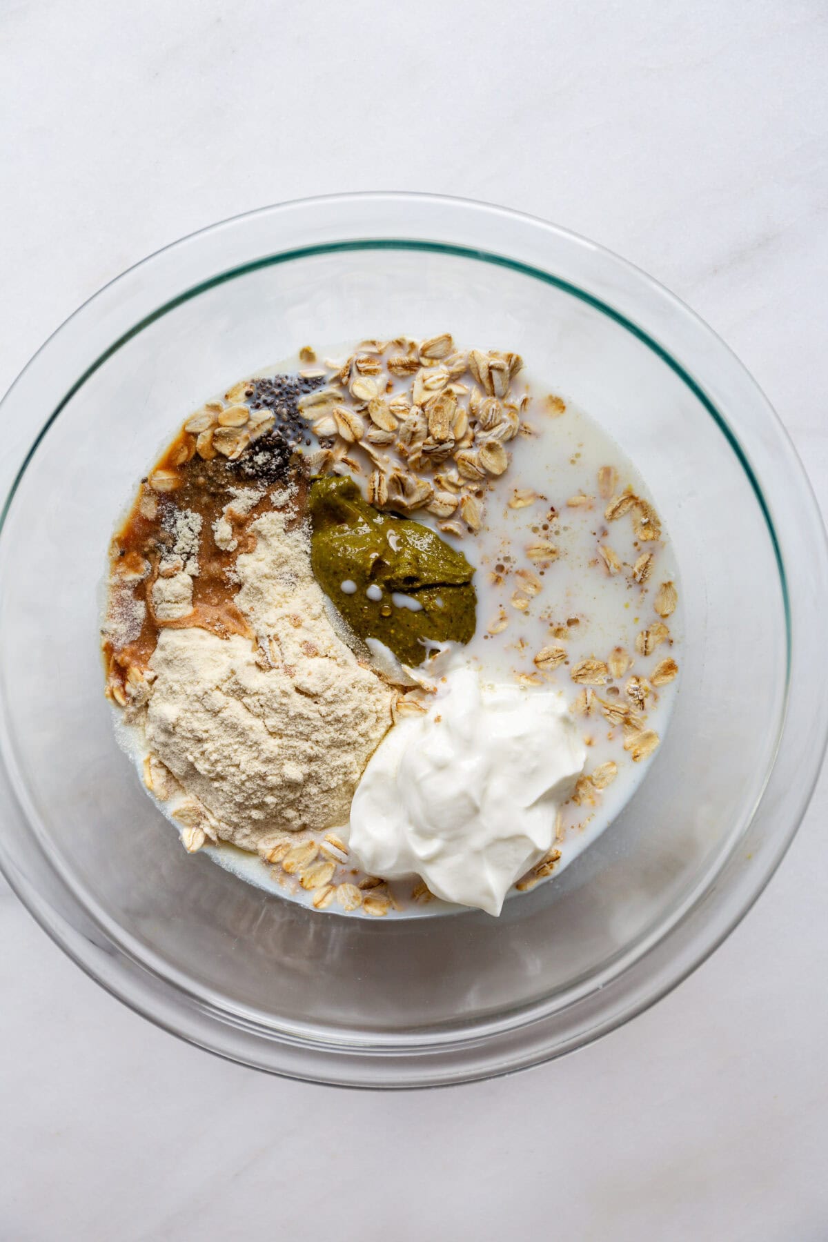 yogurt, protein powder, oats and pistachio butter and almond milk in a clear mixing bowl.