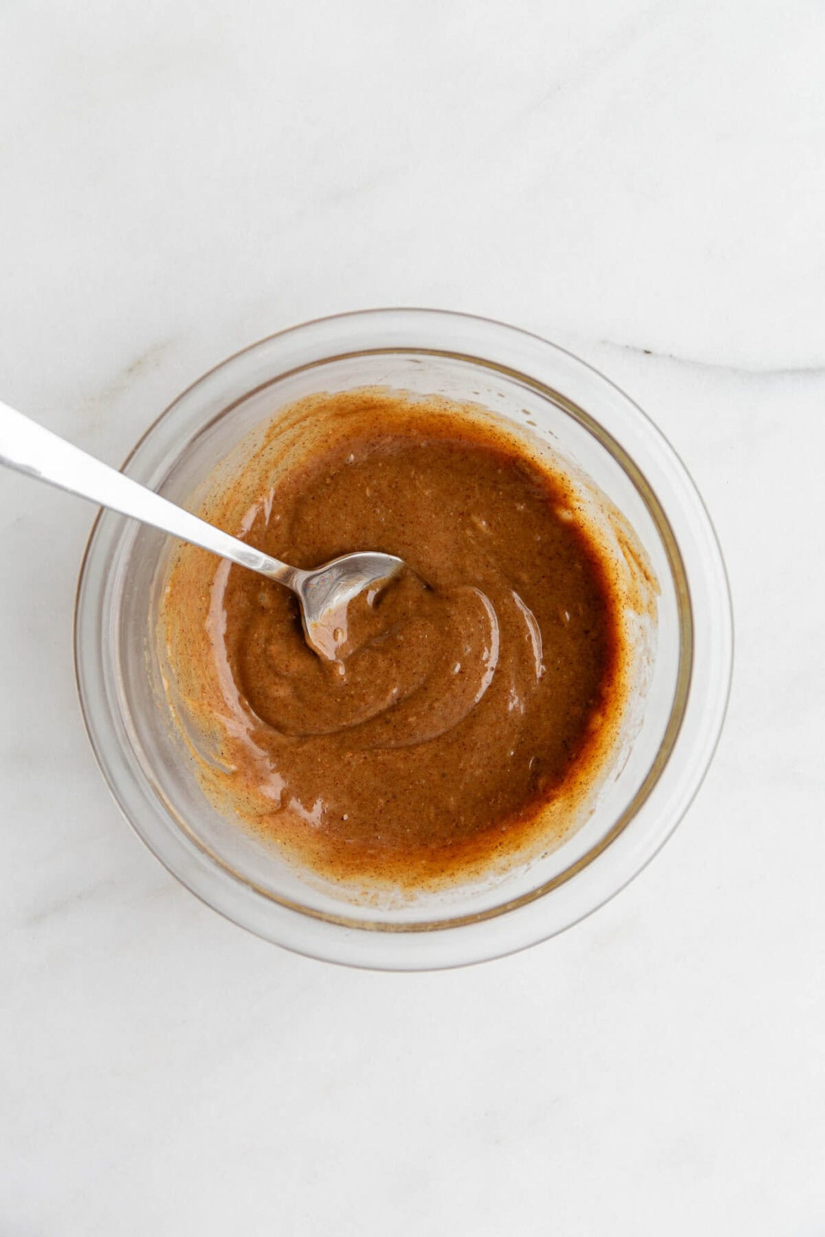 mixed nut butter and maple syrup in a clear mixing bowl with a spoon.