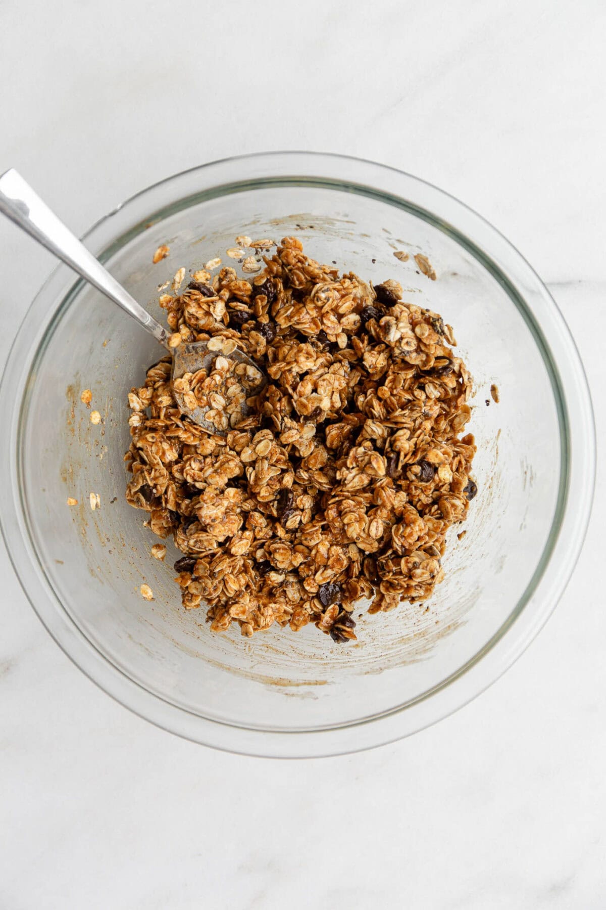 cookie dough granola ingredients in a clear mixing bowl with a spoon.