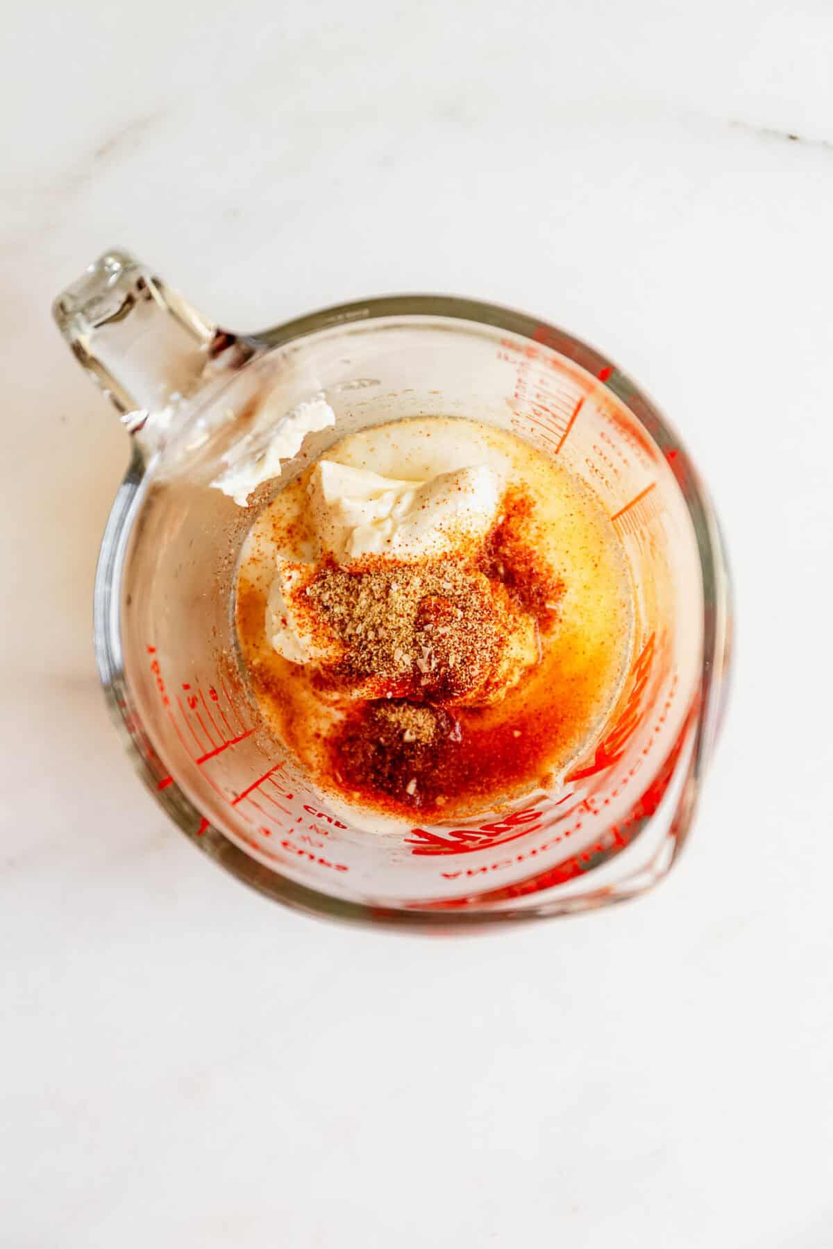Cream cheese and spices in a glass measuring cup for the jalapeno popper chicken salad dressing.