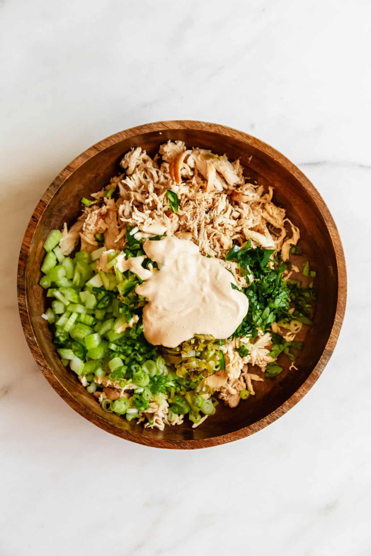 Overhead view of shredded chicken topped with diced green onions and celery in a wooden bowl for jalapeno popper chicken salad.