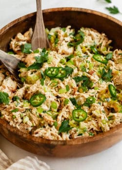 A close-up of jalapeno popper chicken salad in a wooden bowl, topped with sliced jalapeños, green onions, and fresh herbs.