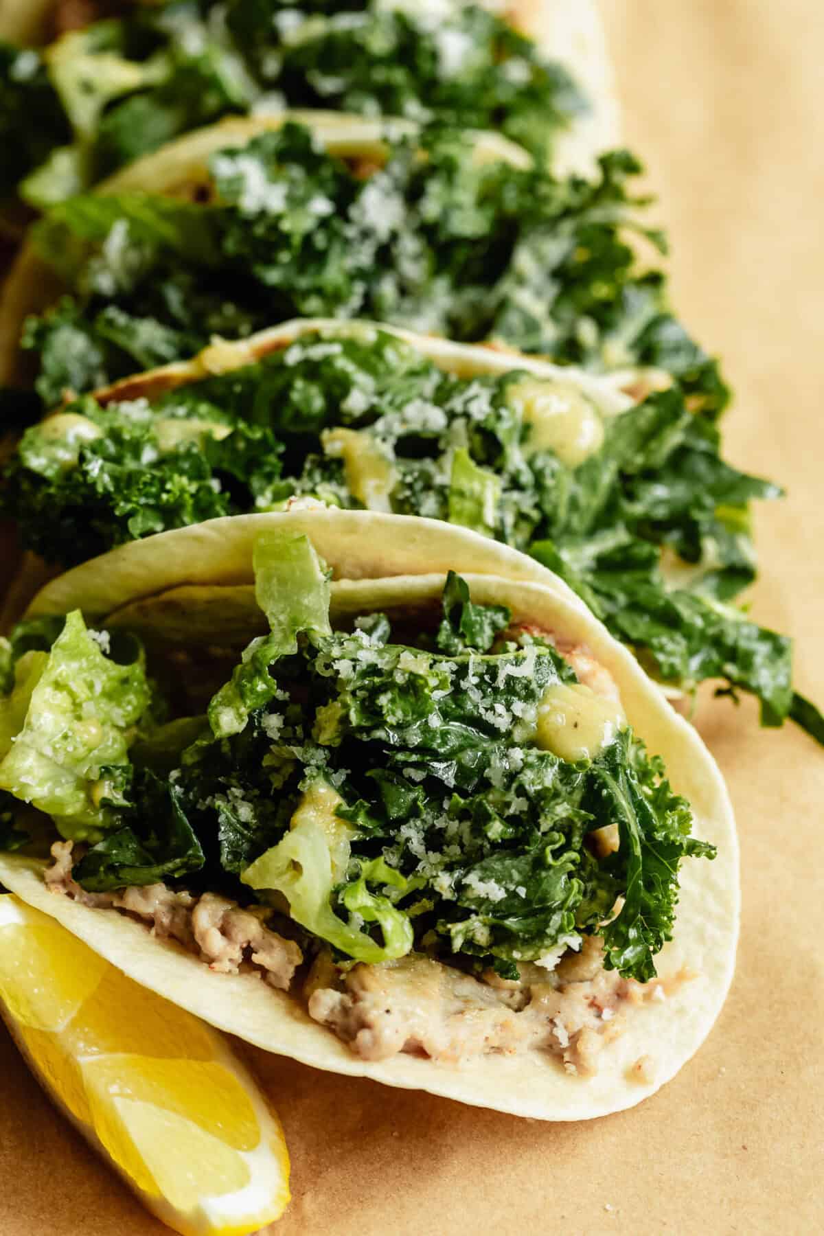 Close-up of chicken caesar smashed tacos loaded with kale caesar salad and parmesan, served with lemon wedges on kraft paper.