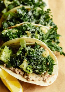 Close-up of chicken caesar smashed tacos loaded with kale caesar salad and parmesan, served with lemon wedges on kraft paper.