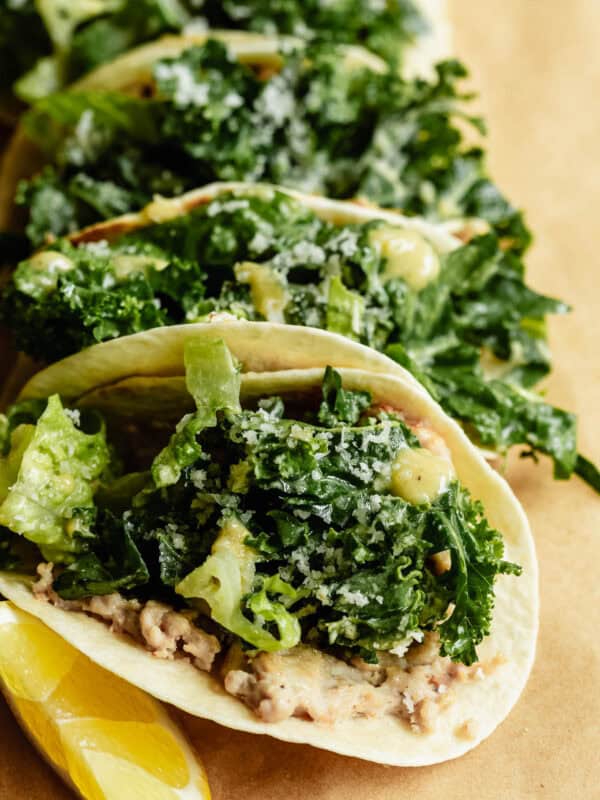 Close-up of chicken caesar smashed tacos loaded with kale caesar salad and parmesan, served with lemon wedges on kraft paper.