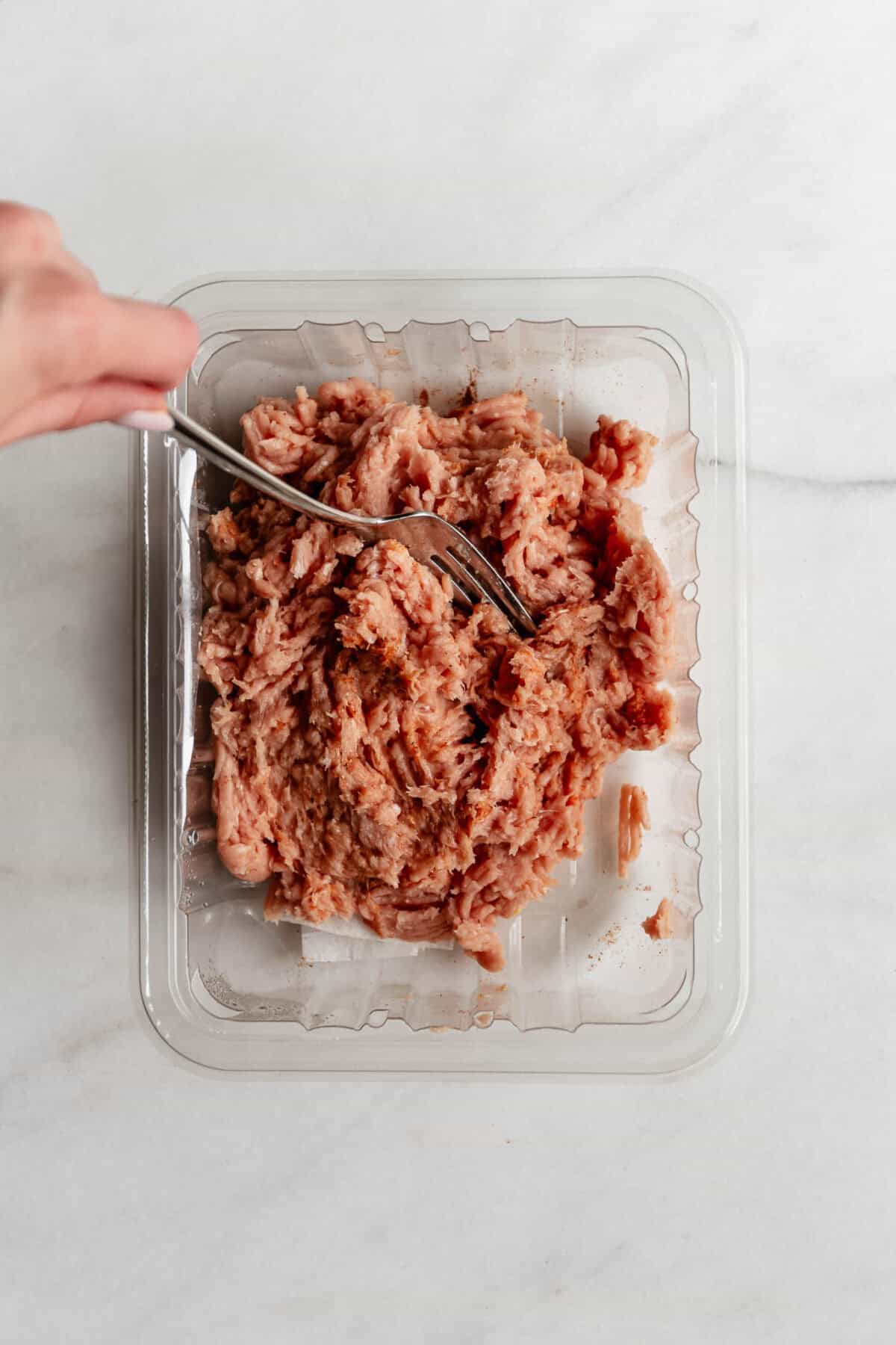 Hand mixing seasoned ground chicken in a plastic container with a fork to prepare for chicken caesar smashed tacos.