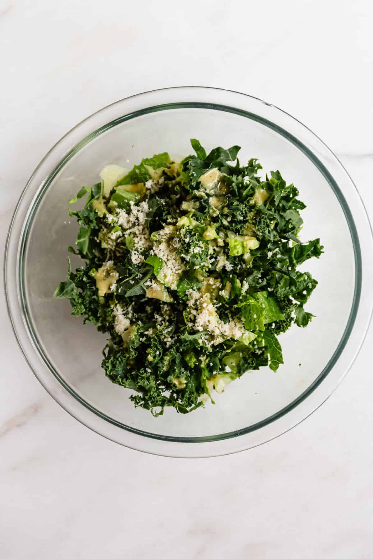 Kale caesar salad with parmesan cheese in a glass bowl viewed from above, topping for chicken caesar smashed tacos.