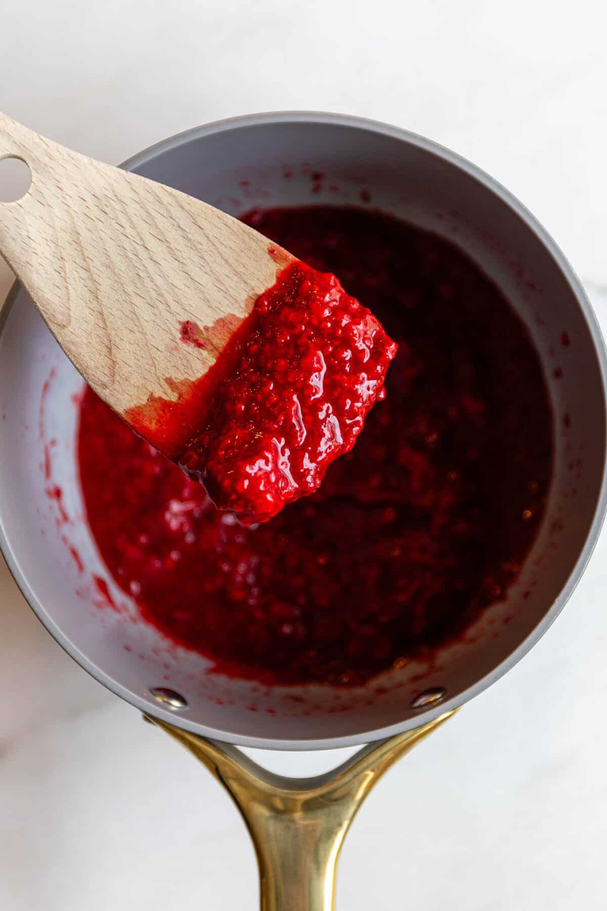 Raspberry chia seed jam being scooped with a wooden spatula in a saucepan.