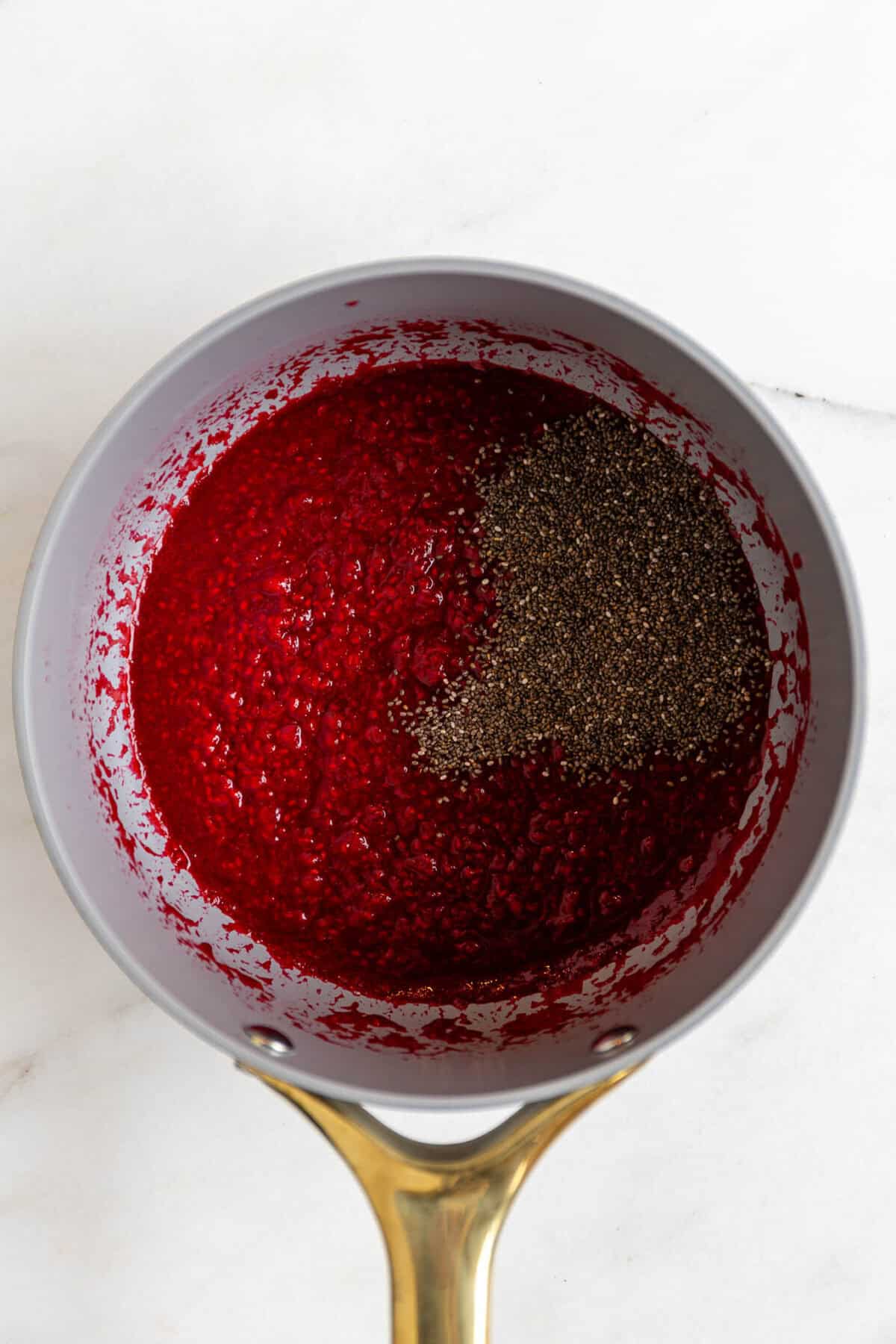Raspberry chia seed jam cooking in a saucepan with chia seeds added.
