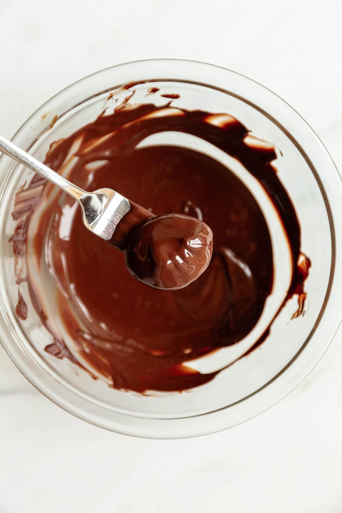a chia jam bite dipped into a bowl of dark chocolate.