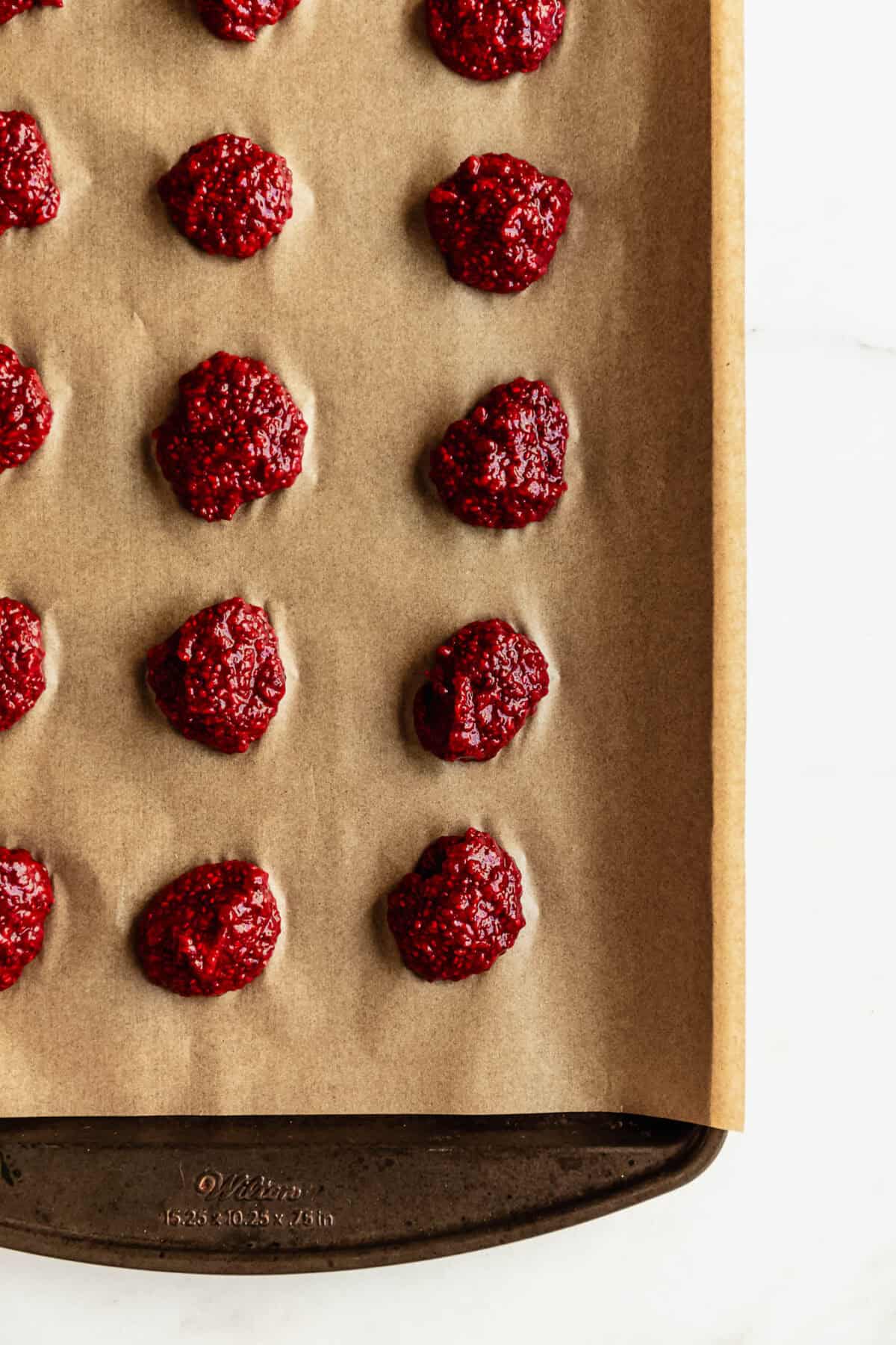 Raspberry chia seed jam bites rolled into balls and placed on parchment paper on a baking sheet.