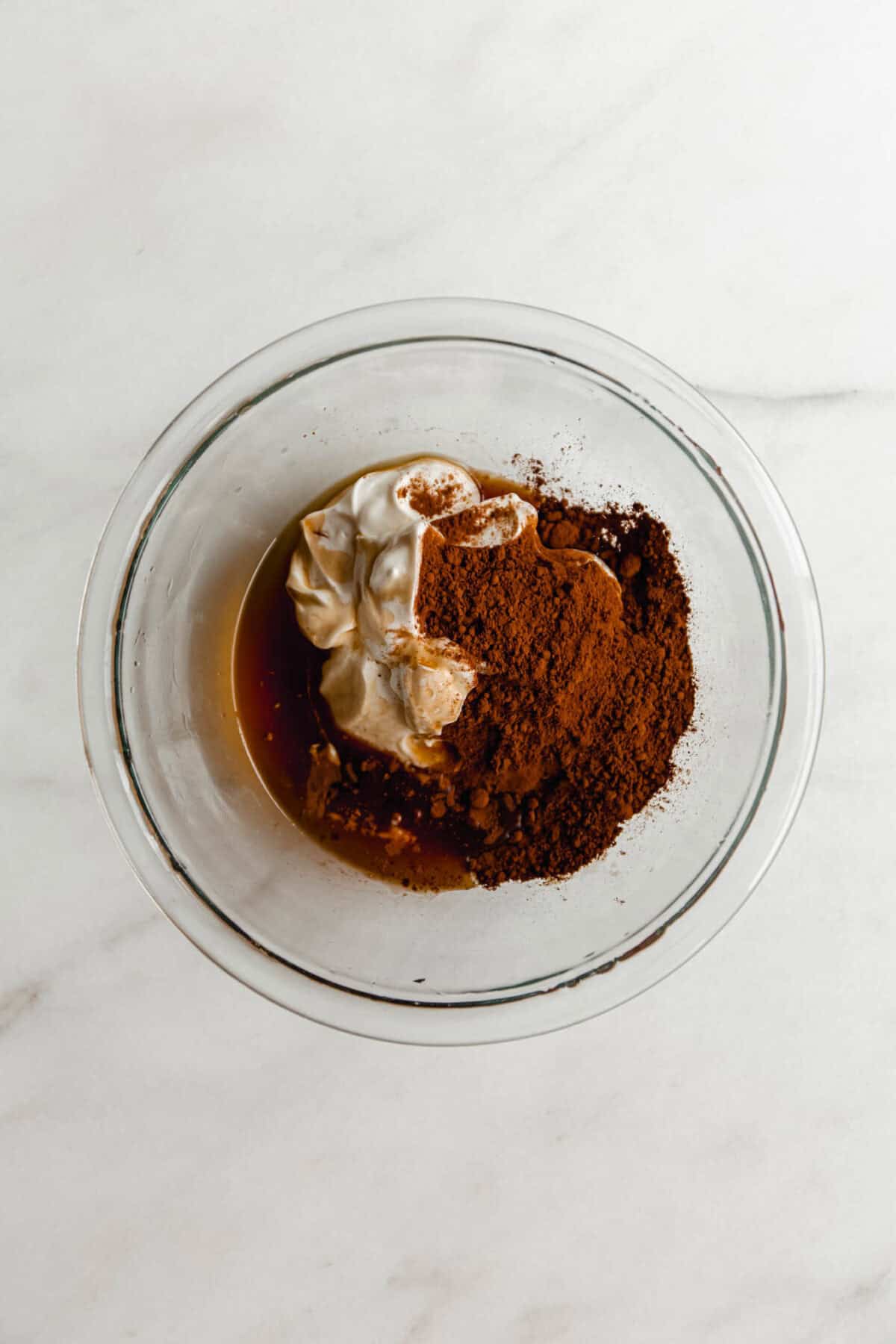 Ingredients for Greek yogurt chocolate mousse in a glass bowl before mixing, including Greek yogurt, cocoa powder, and maple syrup.