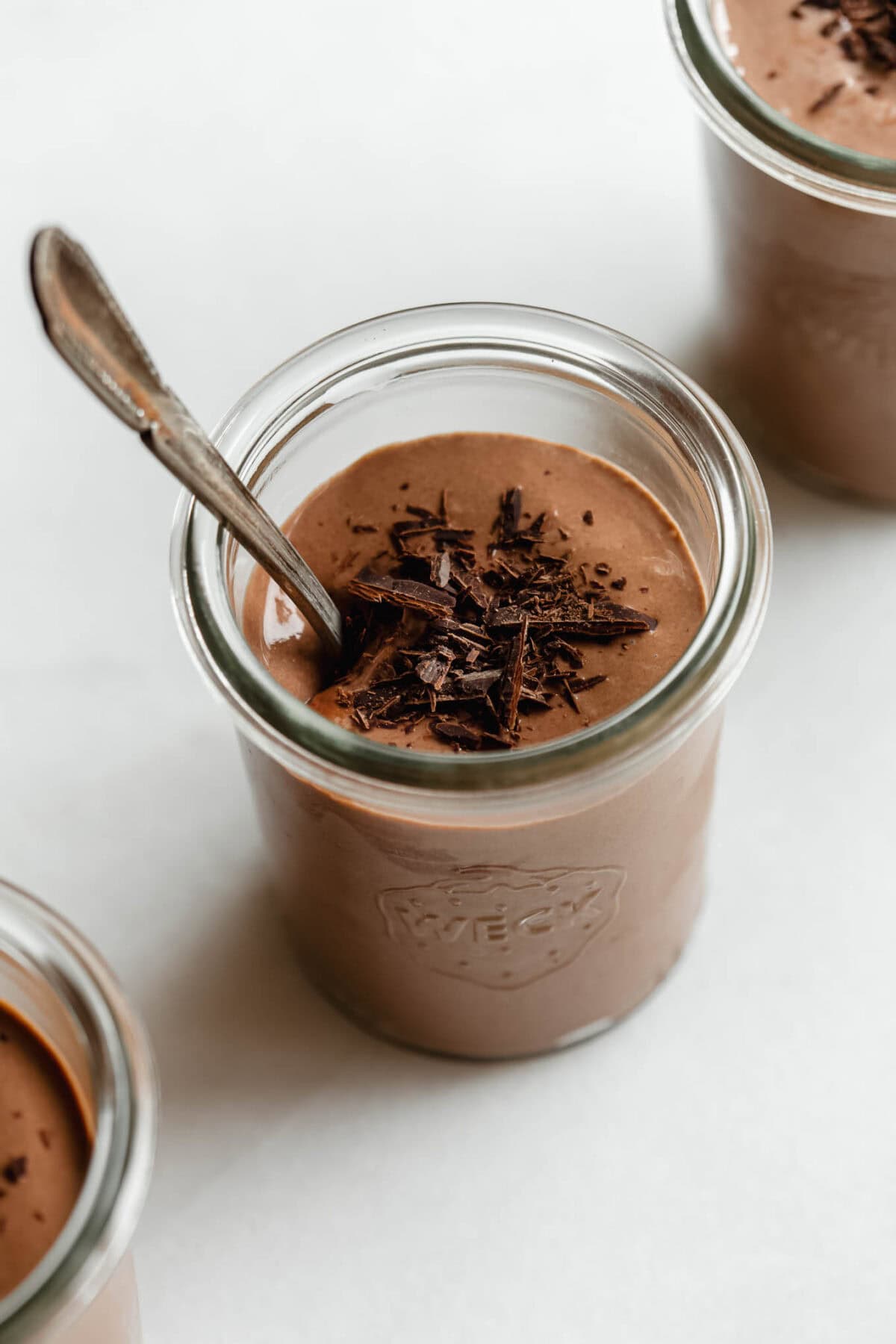 Greek yogurt chocolate mousse served in glass jars topped with chocolate shavings and a spoon.