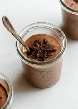 Greek yogurt chocolate mousse served in glass jars topped with chocolate shavings and a spoon.