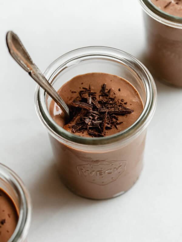 Greek yogurt chocolate mousse served in glass jars topped with chocolate shavings and a spoon.