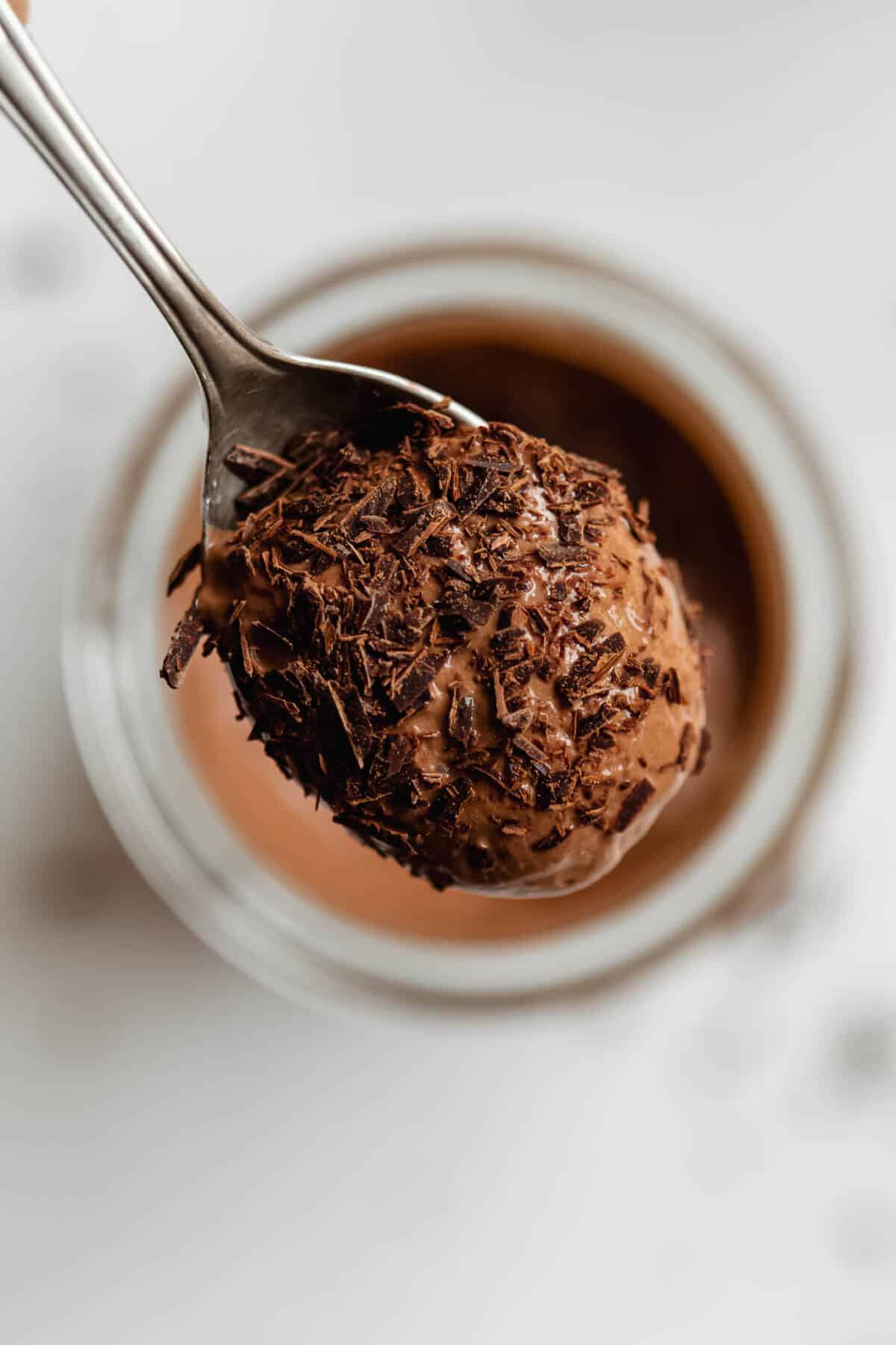 Close-up of Greek yogurt chocolate mousse in a glass jar piled high with chocolate shavings and a spoon.