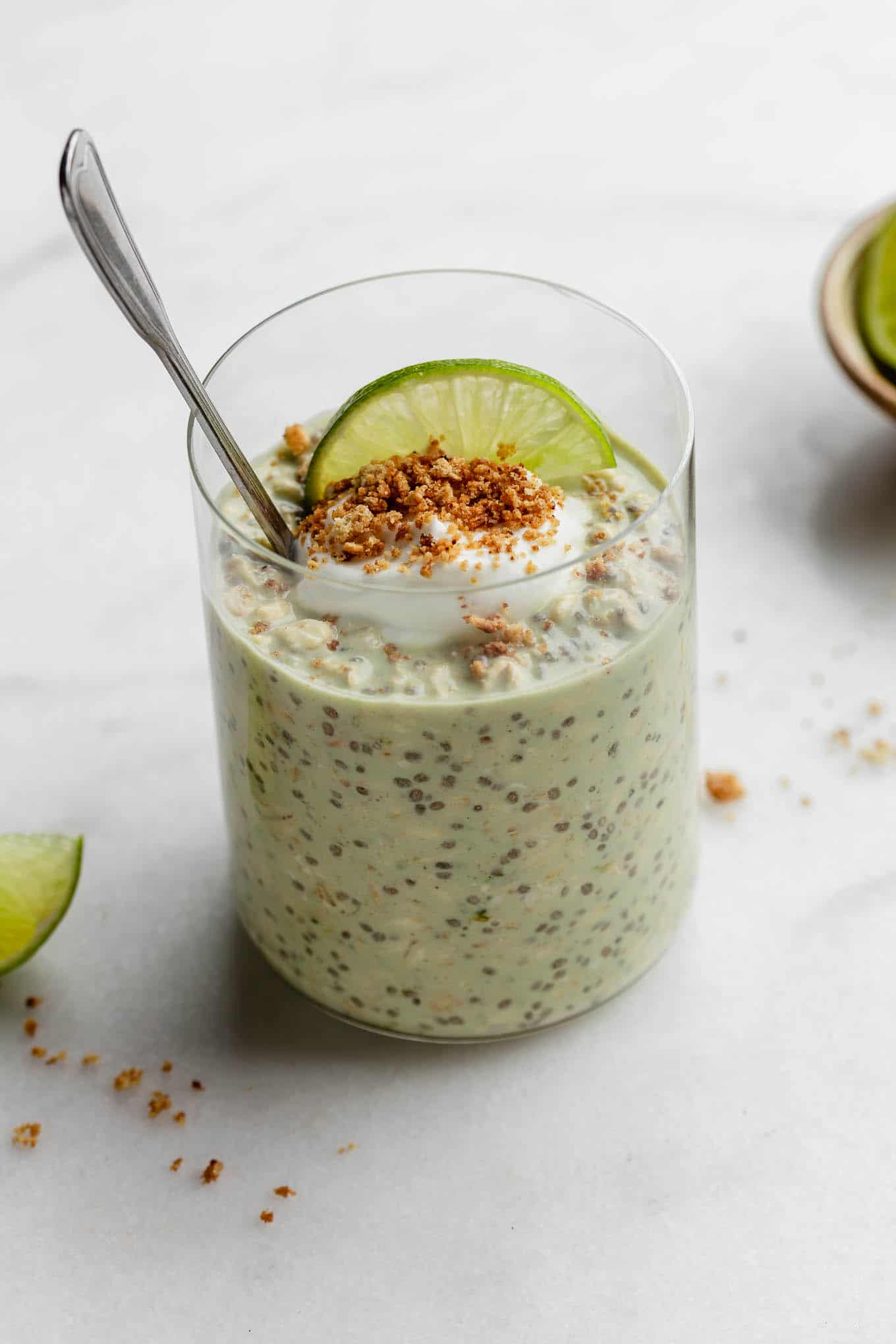 Key lime pie overnight oats topped with yogurt and graham cracker crumbs with a spoon in it.