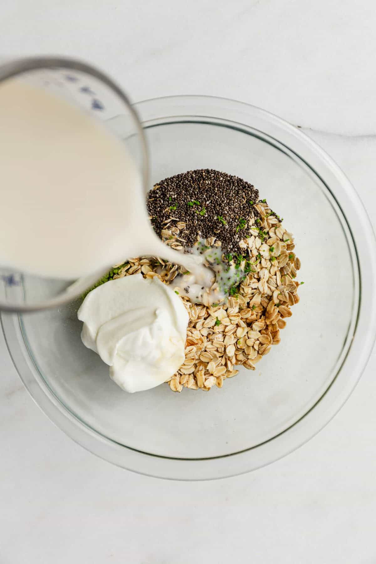 Milk being poured into a bowl of oats, yogurt and chia seeds.