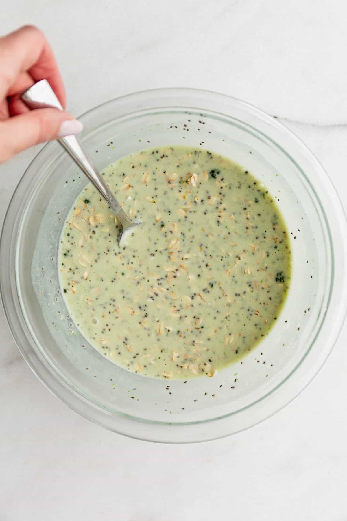a spoon mixing lime overnight oats in a clear mixing bowl.