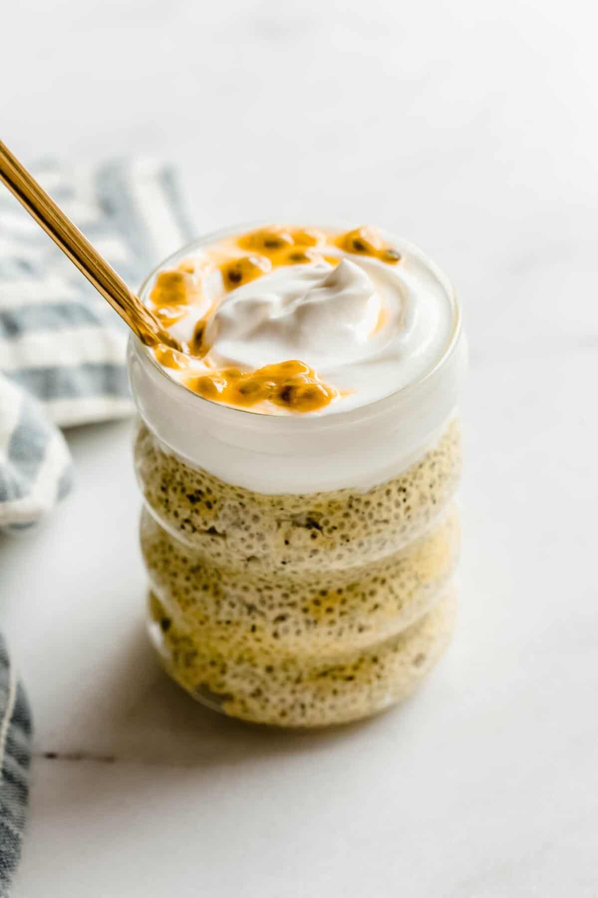 Passionfruit chia pudding in a glass jar topped with creamy yogurt and passionfruit pulp, with a gold spoon.