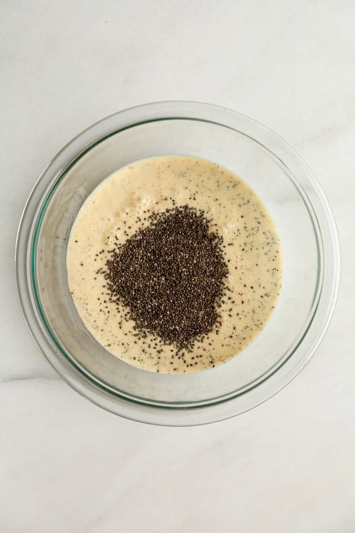Adding chia seeds to the liquid mixture in a bowl for passionfruit chia pudding