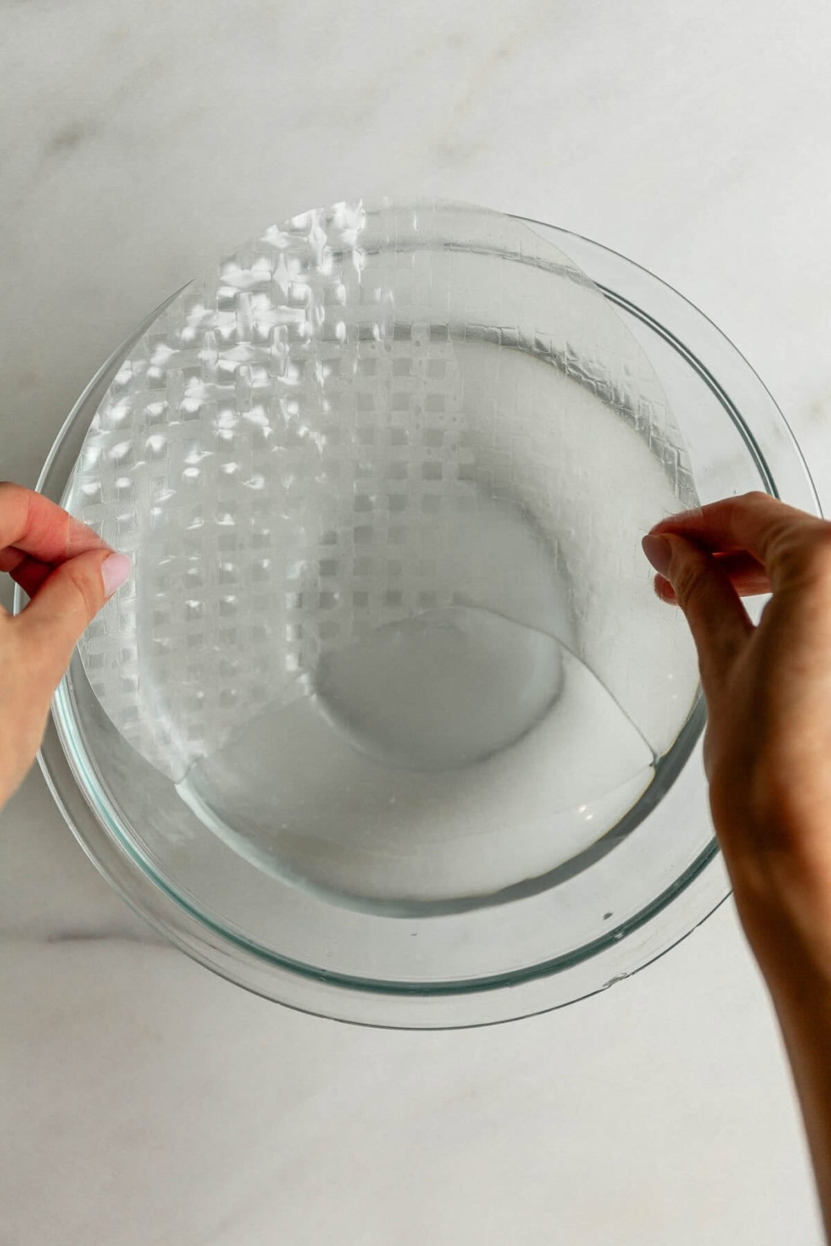Hands soaking a rice paper sheet in a bowl of water to make rice paper mochi