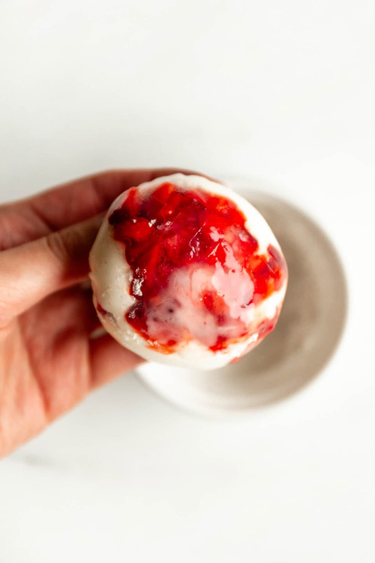 Hand holding a rice paper mochi ball with strawberry filling